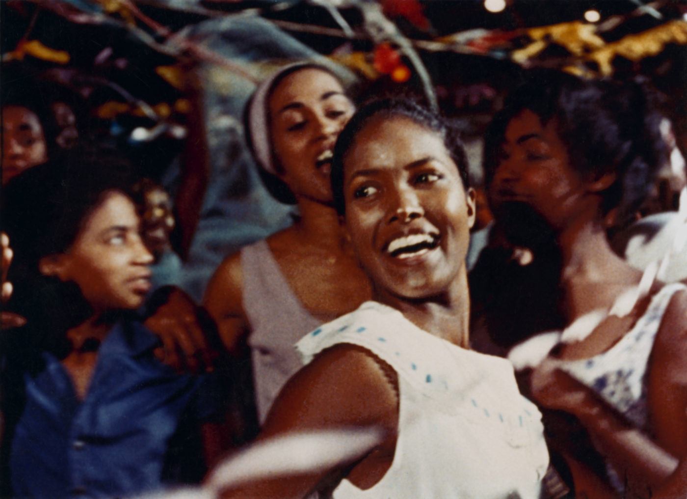 still from Black Orpheus (1959) - a young woman smiles while dancing amid the festivities of mardi gras